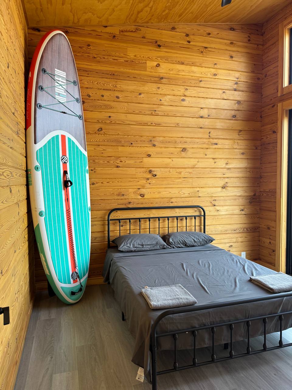Warm timber bedroom with a paddleboard beside the bed